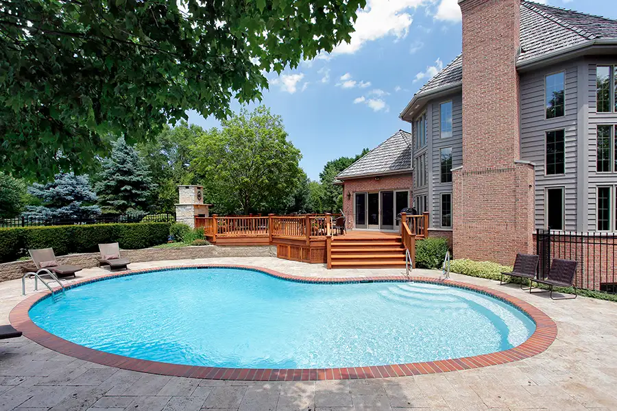 bean-shaped in-ground swimming pool in backyard of lovely home, seating around the pool, deck/patio with seating and fireplace in background - Decatur, IL
